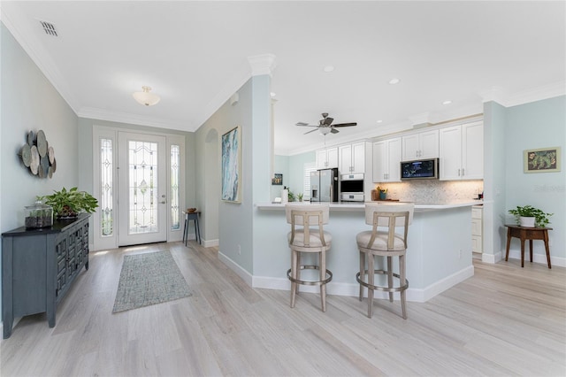 kitchen featuring a kitchen breakfast bar, kitchen peninsula, stainless steel appliances, light wood-type flooring, and white cabinetry