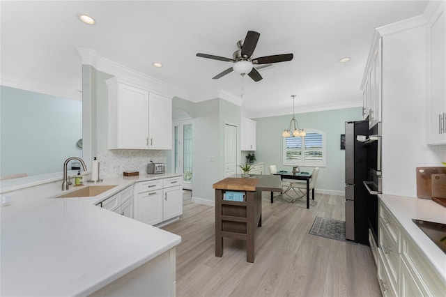 kitchen featuring sink, hanging light fixtures, white cabinets, crown molding, and light hardwood / wood-style flooring