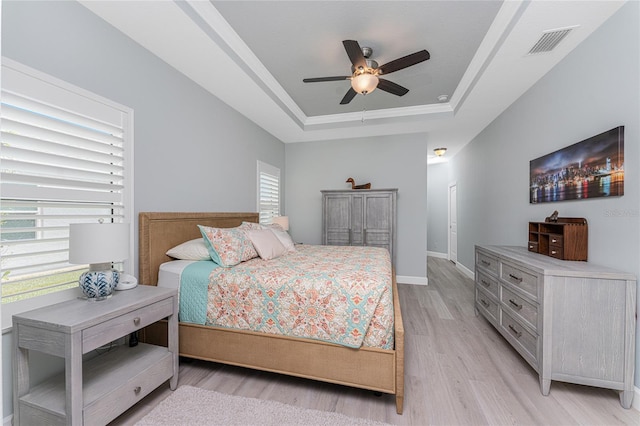 bedroom featuring light hardwood / wood-style flooring, a raised ceiling, and ceiling fan