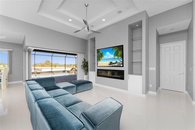 tiled living room featuring a raised ceiling, ceiling fan, built in features, and a wealth of natural light