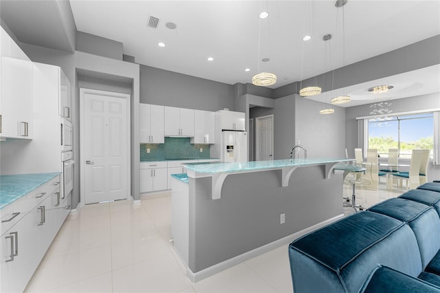 kitchen with an island with sink, white cabinetry, a kitchen breakfast bar, white appliances, and decorative light fixtures