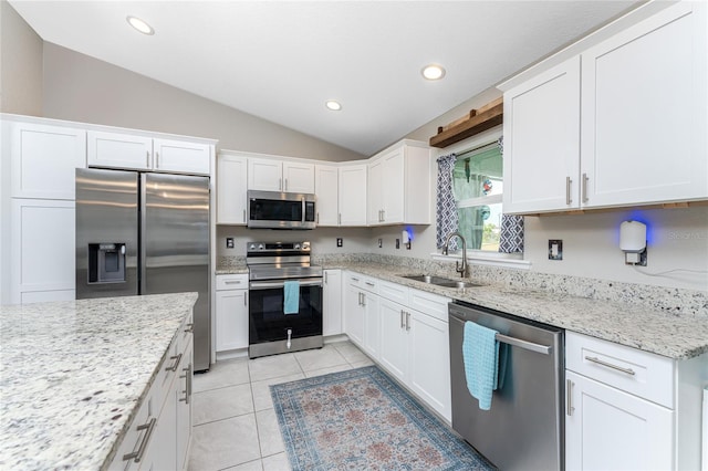 kitchen with white cabinets, light stone counters, vaulted ceiling, sink, and stainless steel appliances