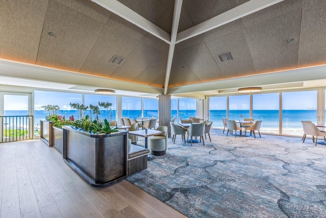 interior space with vaulted ceiling, a water view, a beach view, and hardwood / wood-style flooring