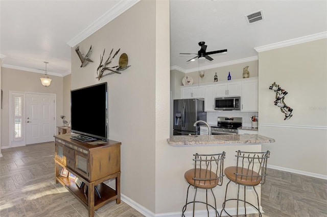 kitchen with ornamental molding, white cabinetry, light stone counters, and stainless steel appliances