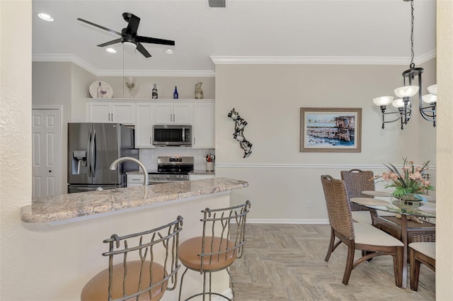 kitchen featuring light parquet flooring, white cabinetry, stainless steel appliances, decorative light fixtures, and a breakfast bar area