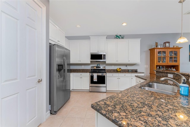 kitchen featuring white cabinets, light tile patterned floors, stainless steel appliances, dark stone counters, and sink