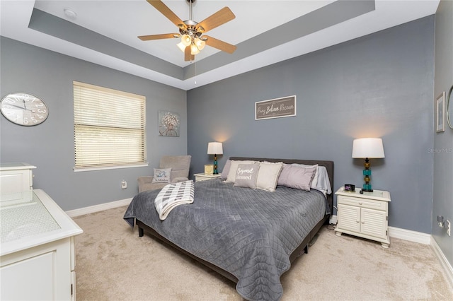 carpeted bedroom with ceiling fan and a raised ceiling