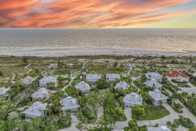 aerial view at dusk featuring a water view and a beach view