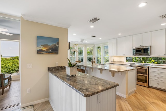 kitchen with stone counters, white cabinetry, ceiling fan, light hardwood / wood-style floors, and appliances with stainless steel finishes