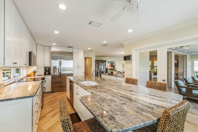 kitchen with white cabinets, appliances with stainless steel finishes, a large island with sink, and sink