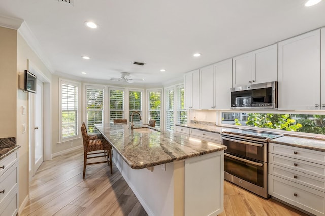 kitchen featuring light hardwood / wood-style floors, a kitchen bar, an island with sink, and appliances with stainless steel finishes