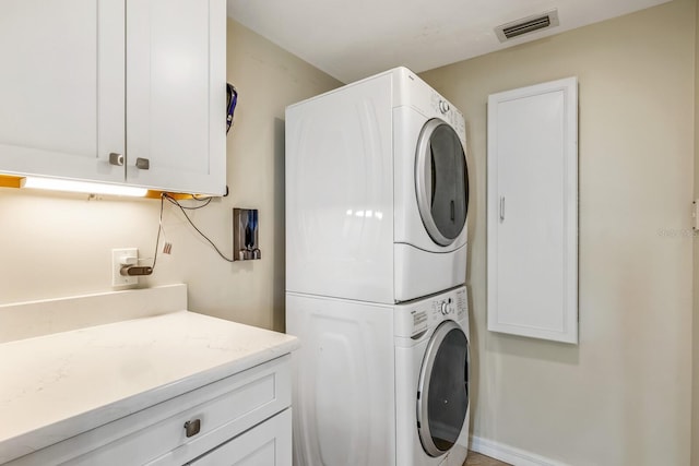 laundry room featuring cabinets and stacked washer / dryer