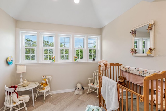 bedroom with light hardwood / wood-style floors, vaulted ceiling, and a nursery area