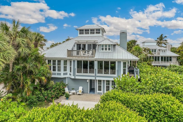 22 Seawatch Dr, Boca Grande, FL 33921 - back of property featuring a balcony, a chimney, a patio area, a metal roof, and a standing seam roof
