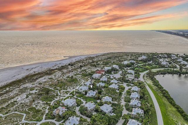 aerial view at dusk with a water view and a view of the beach