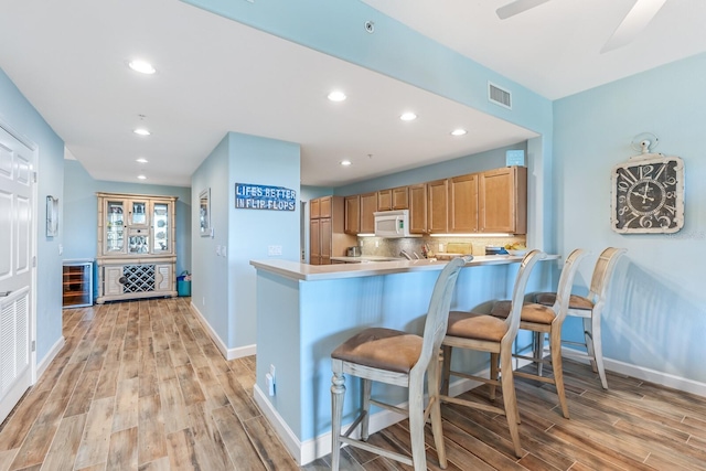 kitchen featuring backsplash, a kitchen breakfast bar, ceiling fan, light wood-type flooring, and kitchen peninsula