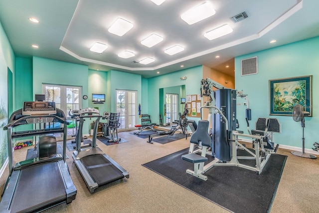 workout area with a towering ceiling, a tray ceiling, and french doors