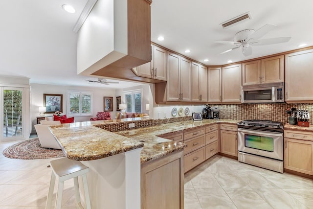 kitchen with plenty of natural light, a kitchen bar, kitchen peninsula, and appliances with stainless steel finishes