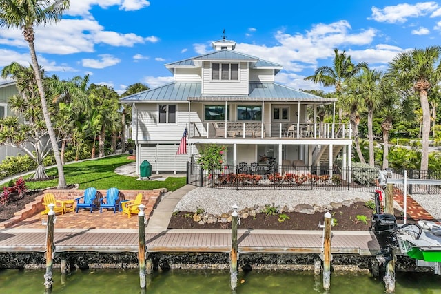 back of property with a balcony, a yard, a patio, and a water view