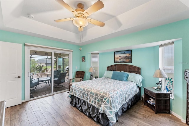 bedroom featuring a raised ceiling, access to exterior, hardwood / wood-style floors, and ceiling fan