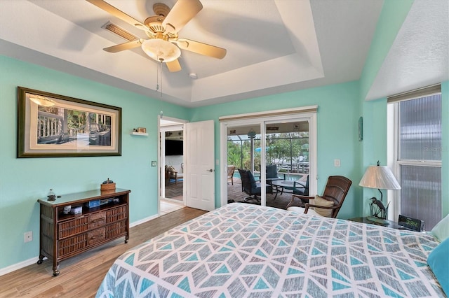 bedroom featuring access to exterior, ceiling fan, hardwood / wood-style floors, and a raised ceiling