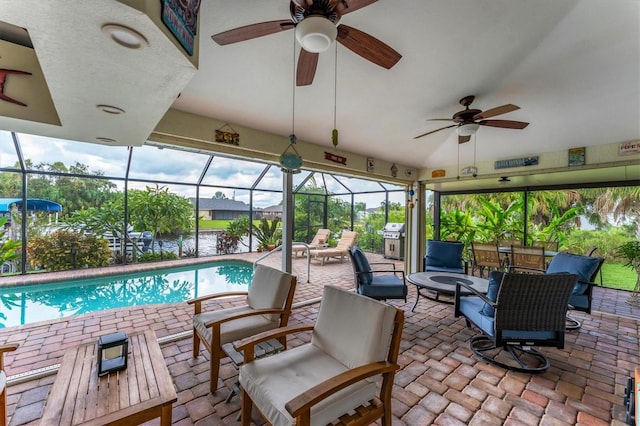 view of swimming pool featuring glass enclosure, ceiling fan, a patio, and grilling area