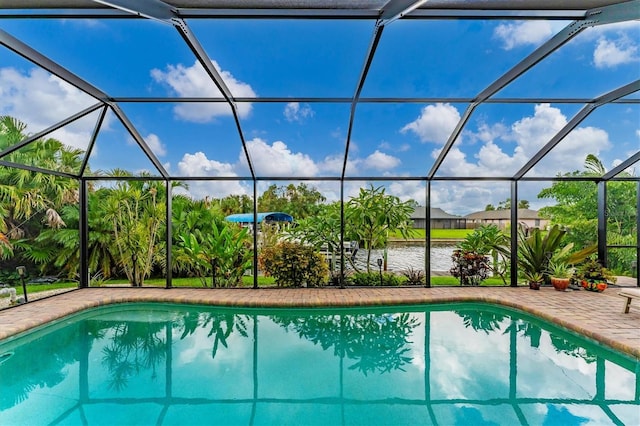 view of pool featuring glass enclosure, a water view, and a patio area