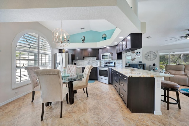 kitchen featuring dark brown cabinets, backsplash, appliances with stainless steel finishes, light stone countertops, and a kitchen bar