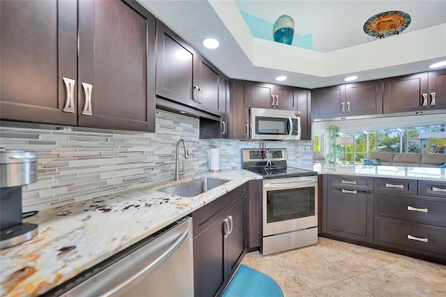 kitchen featuring dark brown cabinets, backsplash, light stone countertops, sink, and stainless steel appliances