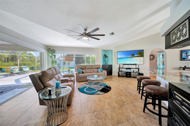 living room with a textured ceiling, ceiling fan, light tile patterned floors, and vaulted ceiling