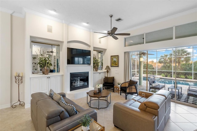 tiled living room with ceiling fan, ornamental molding, and a high ceiling