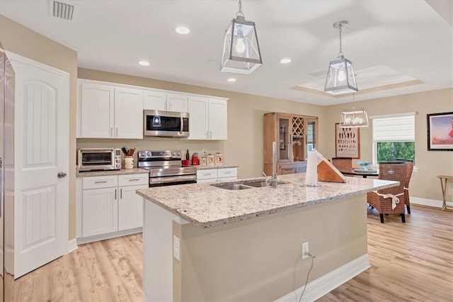 kitchen featuring white cabinets, stainless steel appliances, a kitchen island with sink, and decorative light fixtures