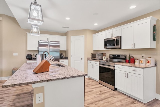 kitchen featuring a kitchen island with sink, stainless steel appliances, white cabinetry, pendant lighting, and light hardwood / wood-style flooring