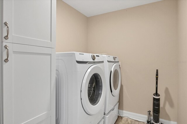 laundry area with light wood-type flooring, washing machine and dryer, and cabinets