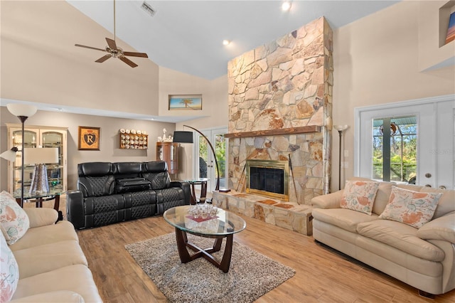 living room with ceiling fan, light hardwood / wood-style floors, a stone fireplace, and high vaulted ceiling