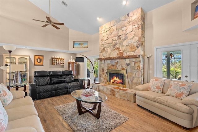 living room featuring ceiling fan, a fireplace, high vaulted ceiling, and light wood-type flooring