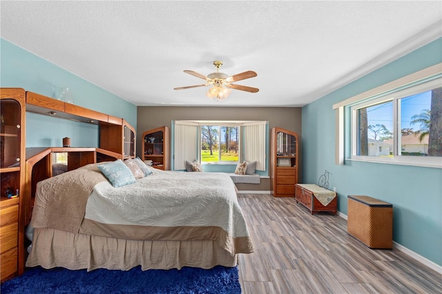 bedroom with ceiling fan, a textured ceiling, wood finished floors, and baseboards