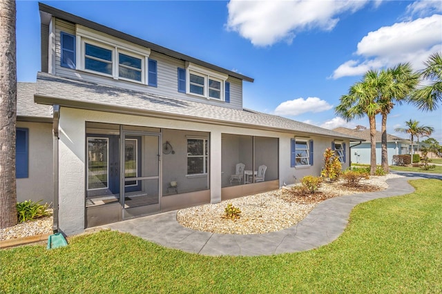 view of front of house with a sunroom, a shingled roof, stucco siding, and a front yard