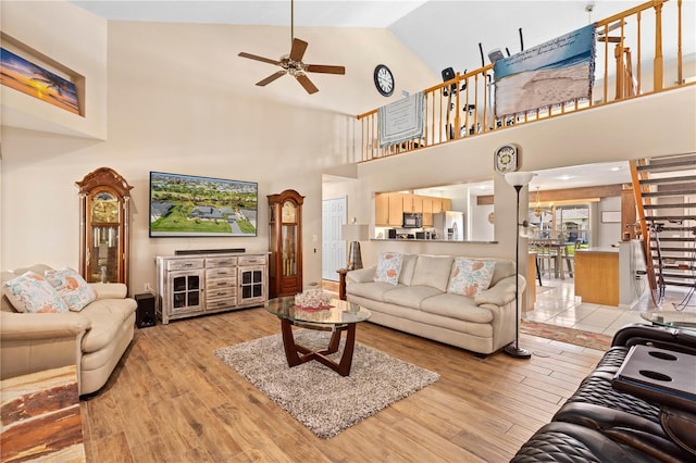 living room featuring high vaulted ceiling, light wood finished floors, stairway, and a ceiling fan