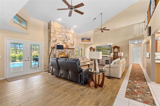 living area with a healthy amount of sunlight, light wood-style flooring, french doors, and a stone fireplace