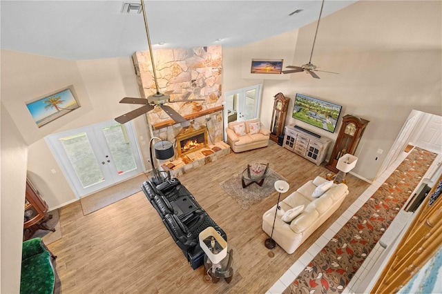 living area with visible vents, wood finished floors, a stone fireplace, french doors, and high vaulted ceiling