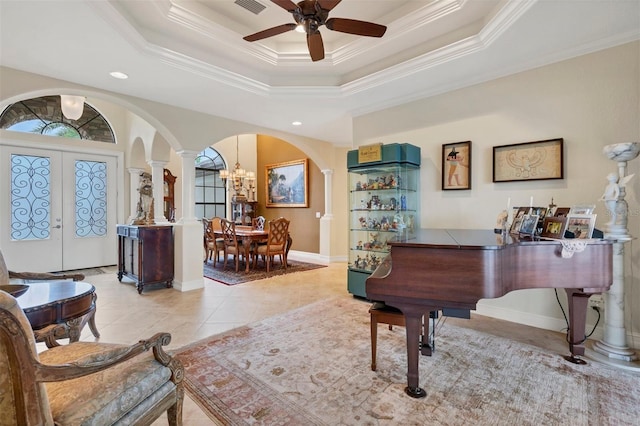 tiled foyer with ornate columns, ceiling fan with notable chandelier, a tray ceiling, french doors, and ornamental molding