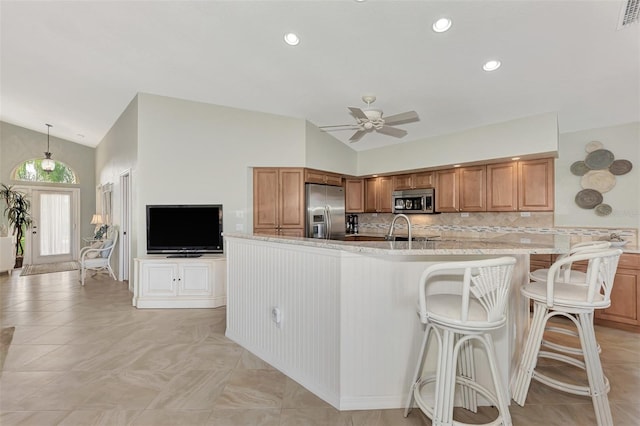 kitchen featuring ceiling fan, brown cabinets, tasteful backsplash, vaulted ceiling, and stainless steel appliances
