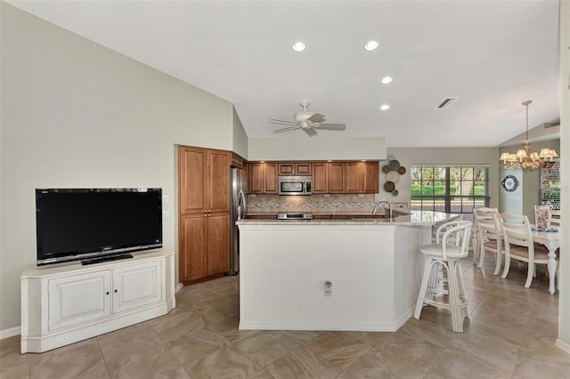 kitchen with lofted ceiling, appliances with stainless steel finishes, a kitchen bar, decorative light fixtures, and a center island with sink