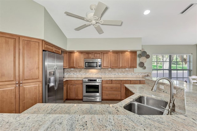 kitchen with tasteful backsplash, vaulted ceiling, sink, light stone countertops, and appliances with stainless steel finishes