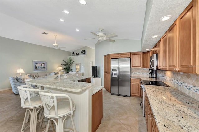 kitchen with light stone countertops, stainless steel appliances, tasteful backsplash, a breakfast bar, and vaulted ceiling