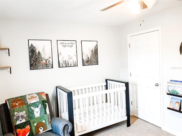 carpeted bedroom with ceiling fan and a crib