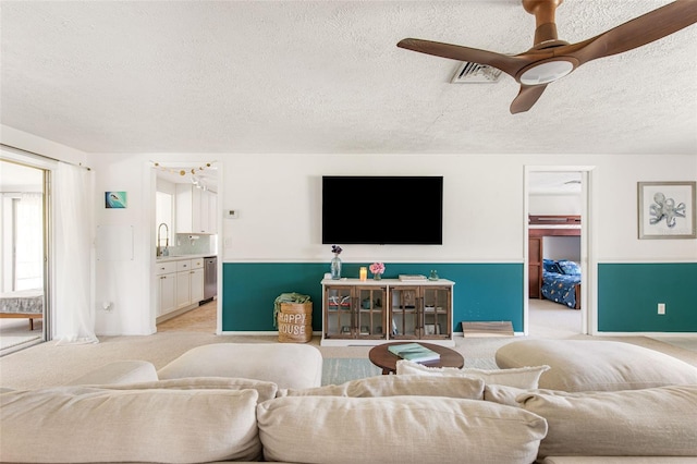 living room featuring light carpet, a textured ceiling, sink, and ceiling fan