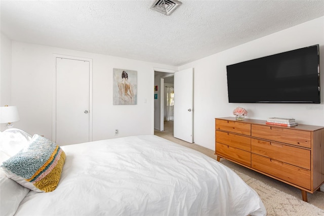 bedroom with a textured ceiling, light colored carpet, and a closet