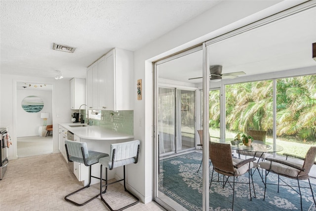 interior space featuring sink, a breakfast bar, tasteful backsplash, white cabinetry, and ceiling fan